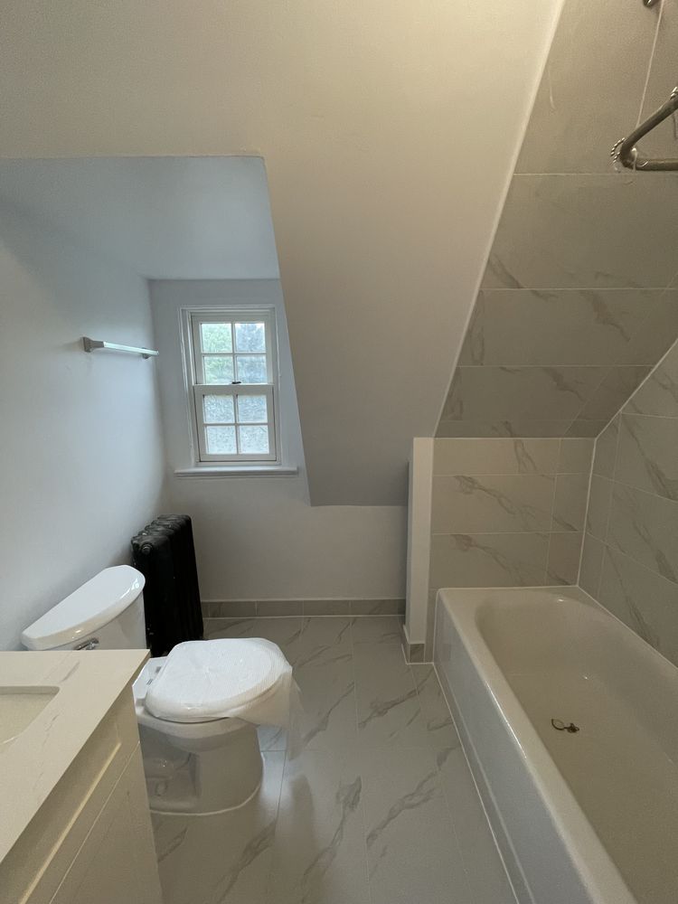 Renovated bathroom with marble-look tile floor, tiled tub surround, toilet and vanity