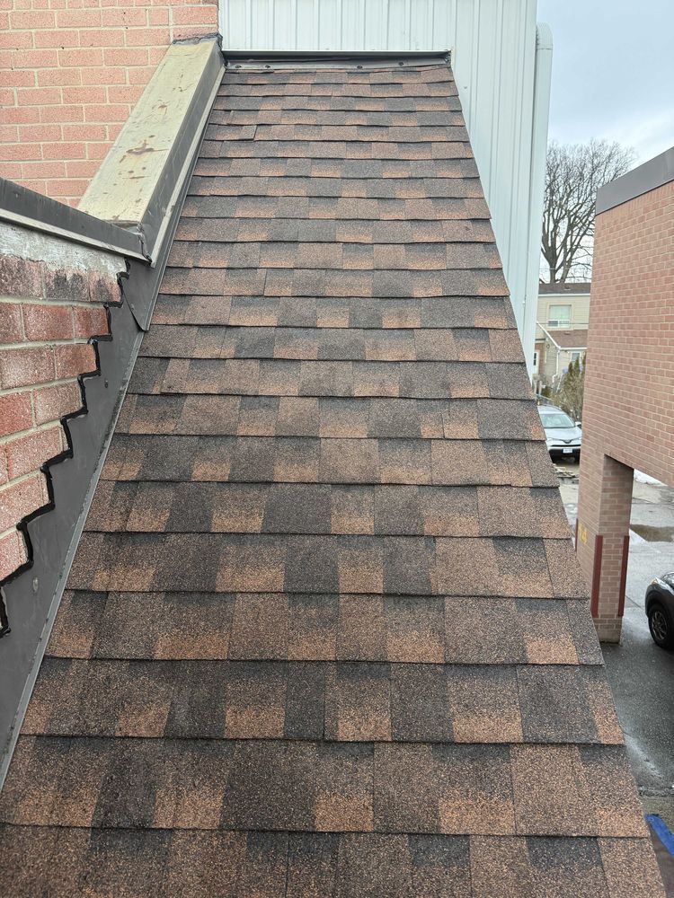 New asphalt shingle roof section with metal flashing along a brick wall